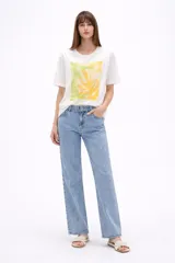 Remera de algodón color blanco, de corte holgado y manga corta, con cuello a la base. Presenta un estampado frontal rectangular en tonos amarillos y verdes con motivos botánicos, realzado con detalles bordados y lentejuelas.