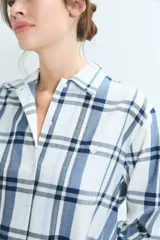 Pijama de dos piezas con estampado de cuadros en tonos azules y blancos. La parte superior es una camisa de manga larga con cuello camisero y cierre frontal de botones. La parte inferior es un pantalón de corte recto con cintura elástica.