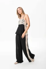 Pantalón sastrero de lino color negro con una guarda lateral de broderie color crudo que recorre el lateral desde la cintura hasta el bajo. El pantalón es de corte ancho y fluido.