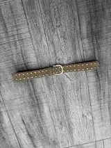 Cinto de gamuza color beige con hebilla plateada y tachas plateadas.