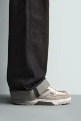 Zapatilla deportiva de cordones, con parte superior en combinación de piezas y materiales en tonos blanco, gris claro y gris oscuro. Suela con volumen.