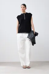 Chaleco negro de tejido de punto con cuello alto, cierre parcial con botones y detalle de pespunte blanco en el ruedo y el cuello. Sin mangas.