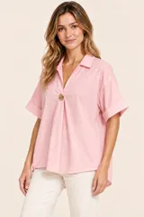Camisa de algodón color rosa con cuello camisero, escote en V con botón decorativo dorado, mangas cortas con vuelta y diseño holgado.