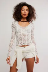 Remera de encaje floral blanca de manga larga y calce ajustado, con escote en V y diseño semitransparente.