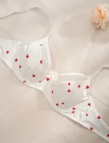 Soutien blanco con estampado de corazones rojos, con breteles finos regulables y moño decorativo en el centro.