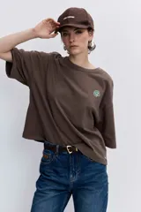 Remera blanca de corte oversize con cuello redondo y mangas cortas, presenta un pequeño bordado de cerezas en el pecho.