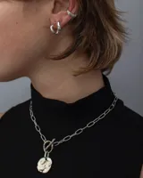 Collar de cadena de eslabones alargados con cierre frontal tipo T y dije circular de textura rústica e irregular.