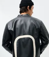 Campera biker de cuero sintético negro con detalles en blanco, cuello mao con broche, cierre frontal y parches bordados en el pecho. Presenta diseño acolchado en los hombros y mangas largas.