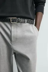 Pantalón de corte slim fit y color negro, confeccionado en tejido elástico. Cuenta con cintura elástica, trabillas, bolsillos frontales y cierre con cremallera y botón.