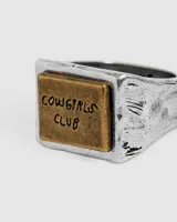 Anillo plateado con aplique rectangular dorado con la inscripción "Cowgirls Club".