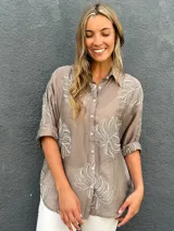 Camisa de seda color visón con bordados en relieve de hojas grandes, cuello camisero, mangas largas y cierre frontal con botones.
