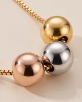 Collar de cadena veneciana de acero con baño dorado, decorado con tres dijes centrales en forma de esfera en tonos oro, plata y oro rosado.