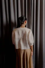 Blusa de lino color gris claro con bordados de pequeñas ramas en tono ocre. Presenta cuello redondo, cartera oculta con botones de nácar y mangas largas con puños estructurados con tablas.
