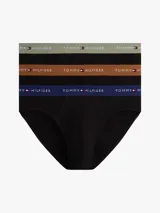 Pack de tres calzoncillos tipo slip de algodón elástico con cintura elástica personalizada con el logo y nombre de la marca Tommy Hilfiger. Cada unidad presenta una banda elástica de distinto color: verde oliva, marrón y azul marino, sobre una base de color negro.