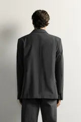 Blazer de corte regular fit color gris oscuro, confeccionado en tejido con lana. Cuenta con cuello con solapas de muesca, cierre frontal con tres botones, bolsillos con solapa en la cadera y un bolsillo de vivo en el pecho.