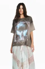 Remera gris de algodón con efecto lavado, corte oversize y estampa frontal gráfica con diseño de alas y texto.