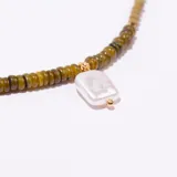 Collar tipo gargantilla con cadena de eslabones dorados y cuentas pequeñas en tonos verde oliva y beige. Posee un dije colgante de nácar o perla de forma cuadrada irregular.