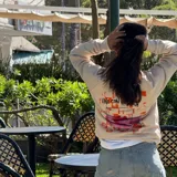 Buzo de cuello redondo en color crema, con diseño estampado en la espalda que incluye un gráfico de una copa con frutillas y la frase 'Vino con frutilla'.