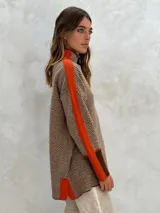 Sweater de punto con patrón de espiga en tonos beige y marrón, cuello alto, mangas largas con detalles en naranja y puños marrones.
