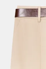 Pantalón tiro bajo color marrón, de corte globo y pernera recta con raya marcada al frente. Incluye trabillas y un cinturón marrón oscuro con hebilla metálica.