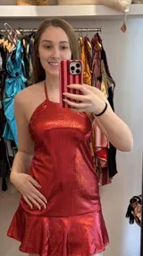 Vestido corto color rojo metalizado, con escote halter, tiras para atar al cuello y falda con volado en el ruedo.