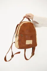 Mochila pequeña de cuero color marrón y beige, con bolsillo externo con cierre, manija superior, bolsillos laterales con broche imán y correas ajustables.
