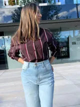 Camisa de corte oversize y manga larga, con diseño de rayas verticales en tonos bordó, blanco y negro. Presenta cuello clásico y cierre frontal con botones.