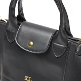 Cartera tipo tote bag de material símil cuero negro, con doble asa corta y correa larga desmontable y regulable. Posee cierre superior metálico, bolsillo interno con cierre y logo XL aplicado en dorado al frente.