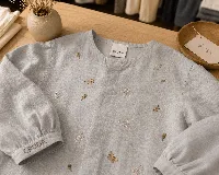 Blusa de lino color gris claro con bordados de pequeñas ramas en tono ocre. Presenta cuello redondo, cartera oculta con botones de nácar y mangas largas con puños estructurados con tablas.