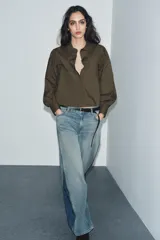 Camisa de popelín color verde militar, con cuello solapa, mangas largas abullonadas terminadas en puño, bajo recto y cierre frontal con botones ocultos por solapa.