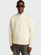 Buzo de algodón de corte holgado, color crema, con cuello redondo y mangas largas. Presenta un diseño minimalista y versátil.