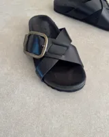 Sandalias negras de cuero con dos tiras anchas cruzadas y hebilla metálica dorada.