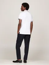 Chomba blanca de algodón elástico, corte slim, con cuello y puños acanalados con ribetes en azul marino y rojo. Tiene cartera de tres botones y logo de Tommy Hilfiger bordado en el pecho.