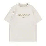 Remera de manga corta color nude, confeccionada en tela tipo gamuza suave, con estampado frontal que incluye el texto "Health Exercise" en dorado y la palabra "PAINS" debajo.