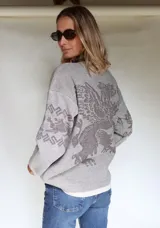 Buzo oversize tejido con diseño jacquard de un grifo en la espalda y detalles geométricos en las mangas. Presenta cuello redondo y puños acanalados.