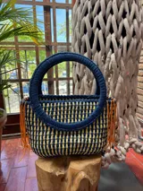 Bolso tejido a crochet con hilo de trapillo en color azul y beige con flecos naranjas y asas circulares rígidas.