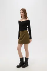 Falda mini de corte recto confeccionada en pana de algodón color verde oliva, con cierre frontal de botón metálico y pasacintos.