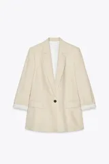 Blazer color beige claro, de corte relajado, con cuello solapa y un solo botón frontal oscuro. Las mangas son de tres cuartos con puños doblados que revelan un forro a rayas blancas y negras.