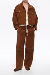 Cazadora corta de corte oversize confeccionada en piel caprina con acabado de ante. Presenta cuello camisero, cierre frontal con botones metálicos, bolsillos con tapeta en el pecho y bolsillos de vivo en el bajo. Incluye mangas largas con pliegues en el codo y puños abotonados.