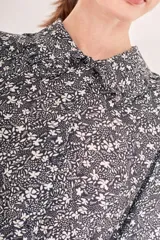 Vestido corto negro con estampado floral pequeño en blanco, cuello camisero, mangas largas abullonadas y cintura ajustable con lazo que termina en borlas negras.