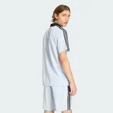 Camiseta deportiva Adidas de manga corta, color celeste con sutiles rayas verticales, cuello polo negro en V y las clásicas tres tiras negras en los hombros. Cuenta con el logotipo de la marca y la inscripción "adidas" en el pecho en color negro.