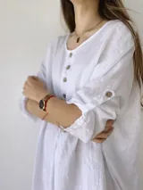 Vestido blanco de lino, corte holgado, con cuello redondo, mangas 3/4 con botones y cierre frontal parcial con botones de madera.