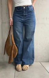 Jean wide leg de tiro medio-alto, color azul con lavado clásico y efecto desgastado. Presenta costuras laterales destacadas que estilizan la silueta, bolsillos delanteros y traseros, y cierre frontal con botón metálico y cremallera.