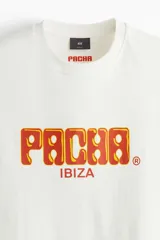 Remera de algodón color blanco con cuello redondo y mangas cortas. Presenta un estampado frontal con el logo de Pacha Ibiza en tonos naranja y amarillo.