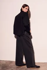 Sobrecamisa negra de estilo shacket, confeccionada en tejido de gamuza sintética. Presenta cuello camisero, cierre frontal de botones y dos bolsillos de parche con solapa en el pecho. El calce es oversize y las mangas son largas.