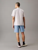 Camisa de manga corta Calvin Klein confeccionada en popelín de algodón elástico con diseño de rayas verticales en tonos beige y blanco. Presenta cuello en punta, cierre frontal de botones, bolsillo de parche en el pecho con logo bordado y bajo recto.