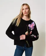 Sweater negro de algodón con cuello redondo, manga larga y corte holgado. Presenta incrustaciones florales decoradas con bordados a mano.
