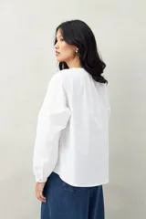 Camisa blanca de algodón con cuello mao con leve frunce, abotonadura frontal con botones de nácar y mangas amplias con puños fruncidos.