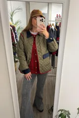 Campera capitoneada color verde oliva con diseño acolchado. Presenta cuello, puños y detalles en los bolsillos de pana en color azul marino, con ribetes en color rojo. Cuenta con cierre frontal mediante botones y ajuste en los puños.