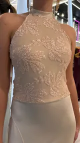 Vestido largo beige, con cuerpo de cuello halter bordado con motivos florales y falda fluida con abertura frontal en la pierna.